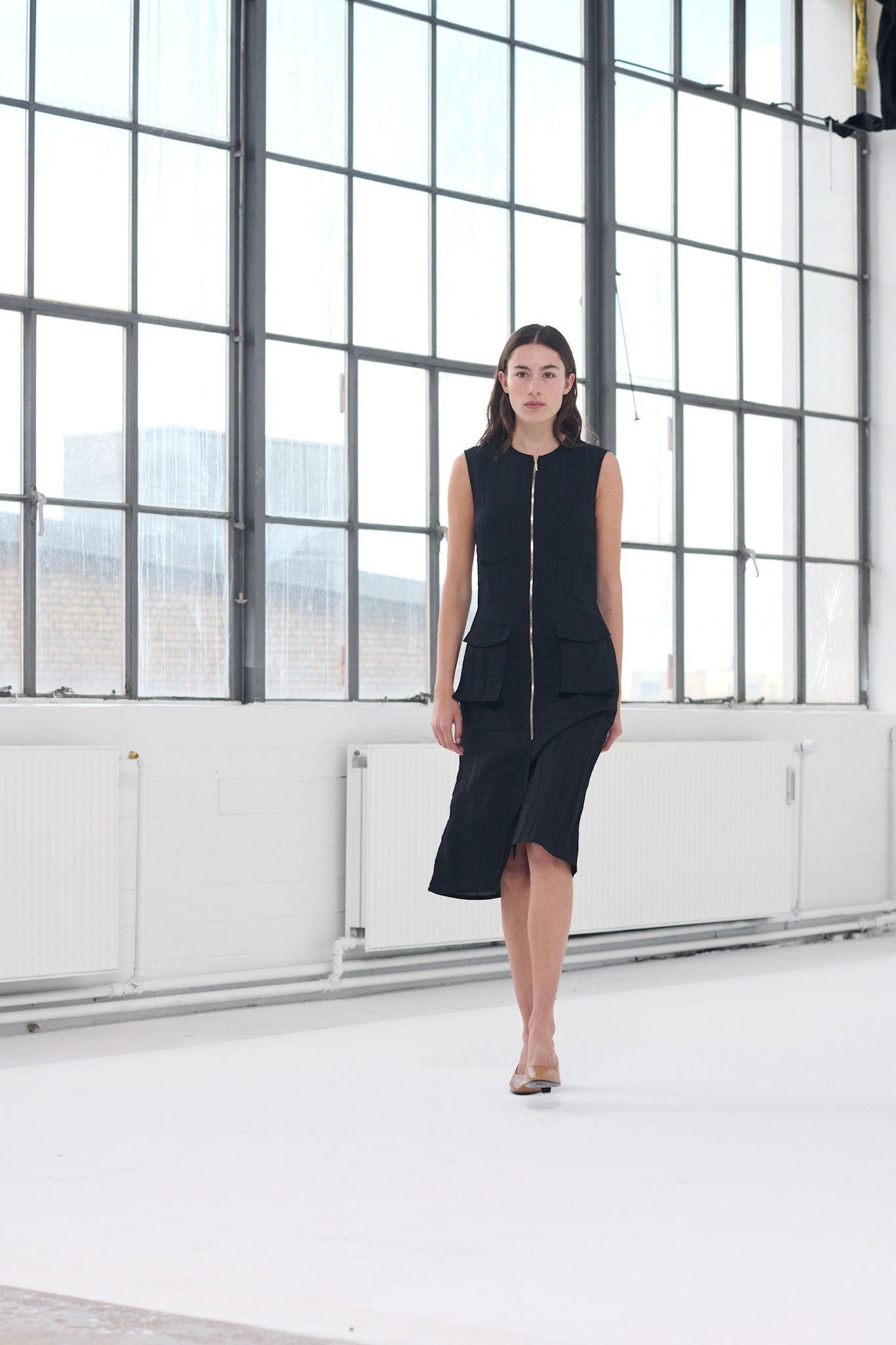 Model wearing the Phoebe Dress, a black sleeveless midi dress with a sleek zip-front design – ideal as an evening midi dress.