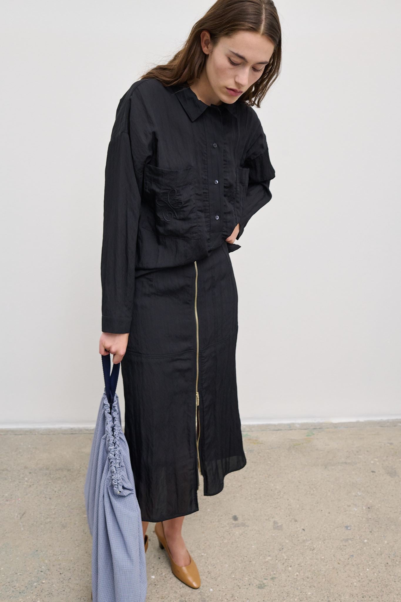 Model wearing Lavigna Skirt, a sleek black midi skirt with a gold zipper and subtle sheen.