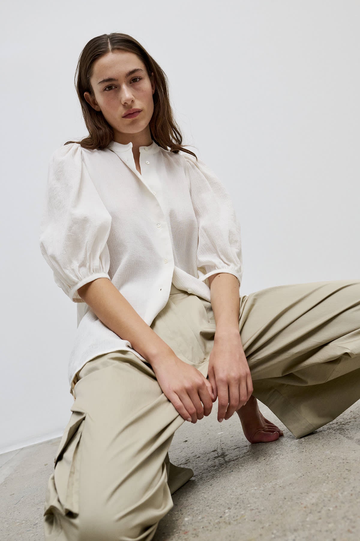 Model styled in the crinkled cotton shirt with puffed shoulders and elbow-length sleeves, paired with relaxed trousers for a modern, effortless look.