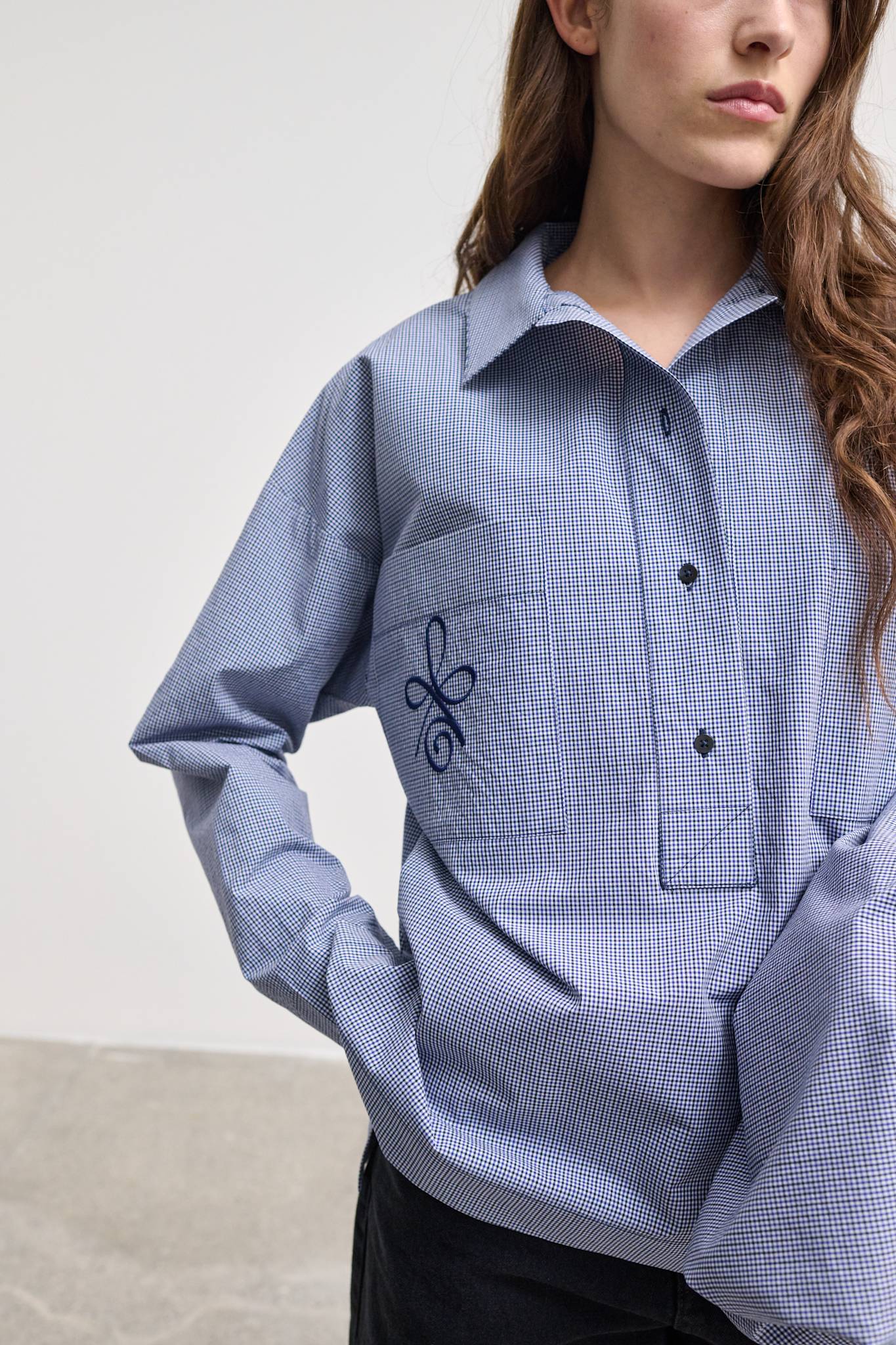 Model wearing Andrea Shirt, a blue checkered half-placket shirt with a relaxed fit and embroidered chest detail.