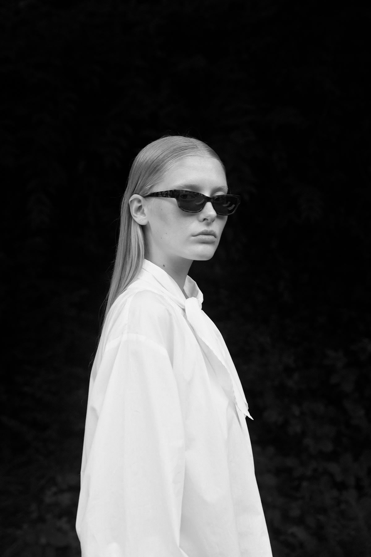 Side view of a model wearing the elegant white blouse with tie, styled with sunglasses.