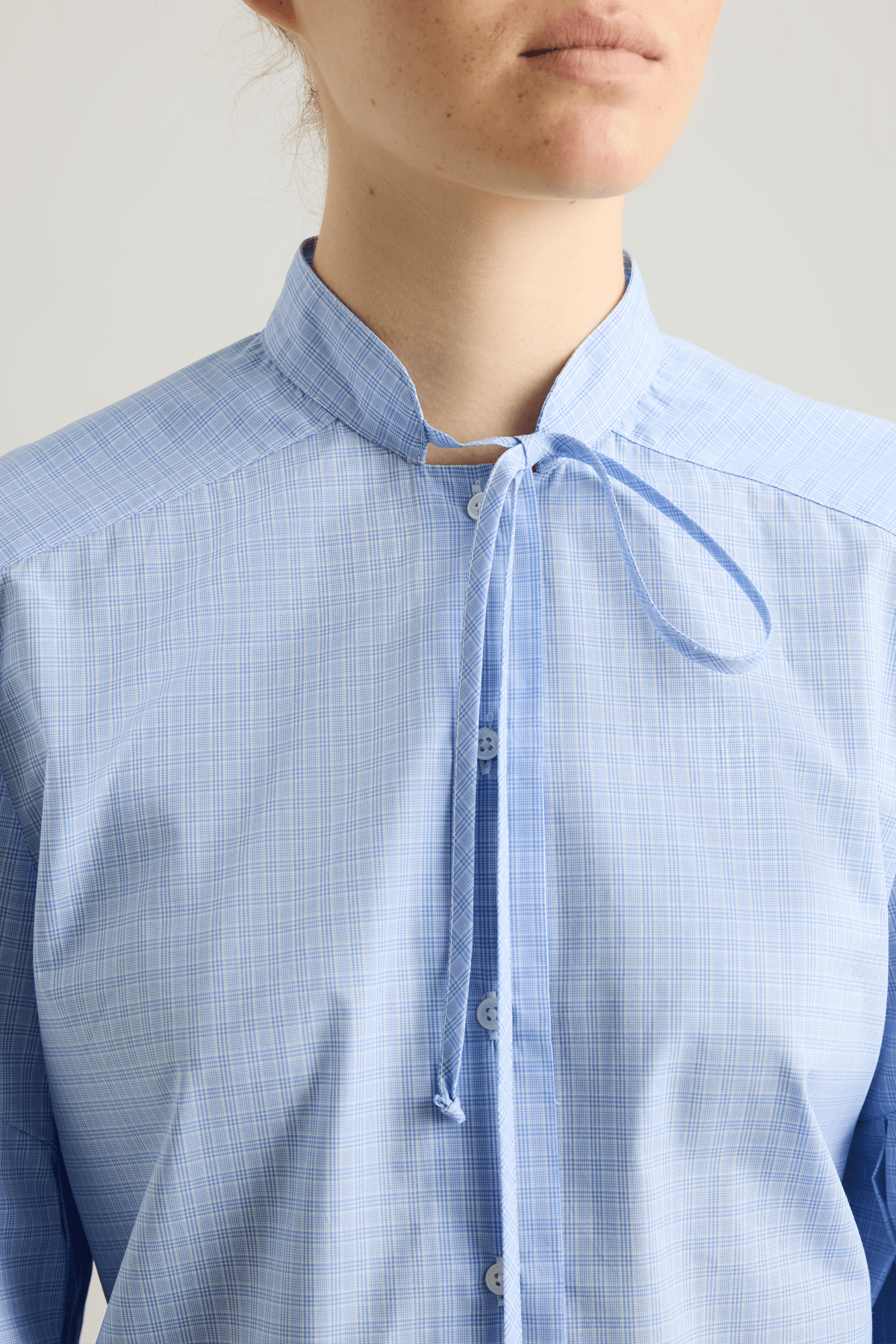 Model wearing Banda shirt in blue check cotton with neck tie and pleated sleeves.
