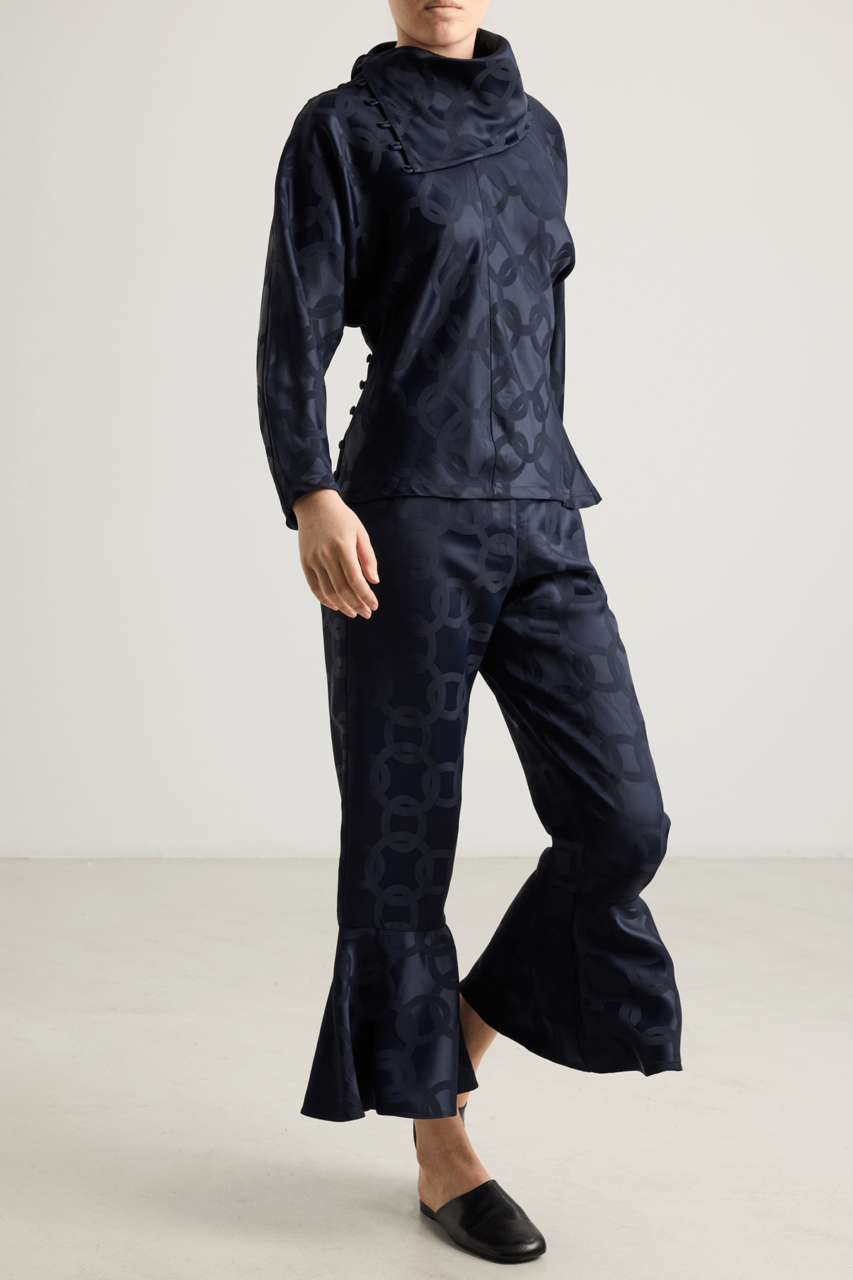 Model wearing Kasey trousers in dark blue satin jacquard with flounced hem.