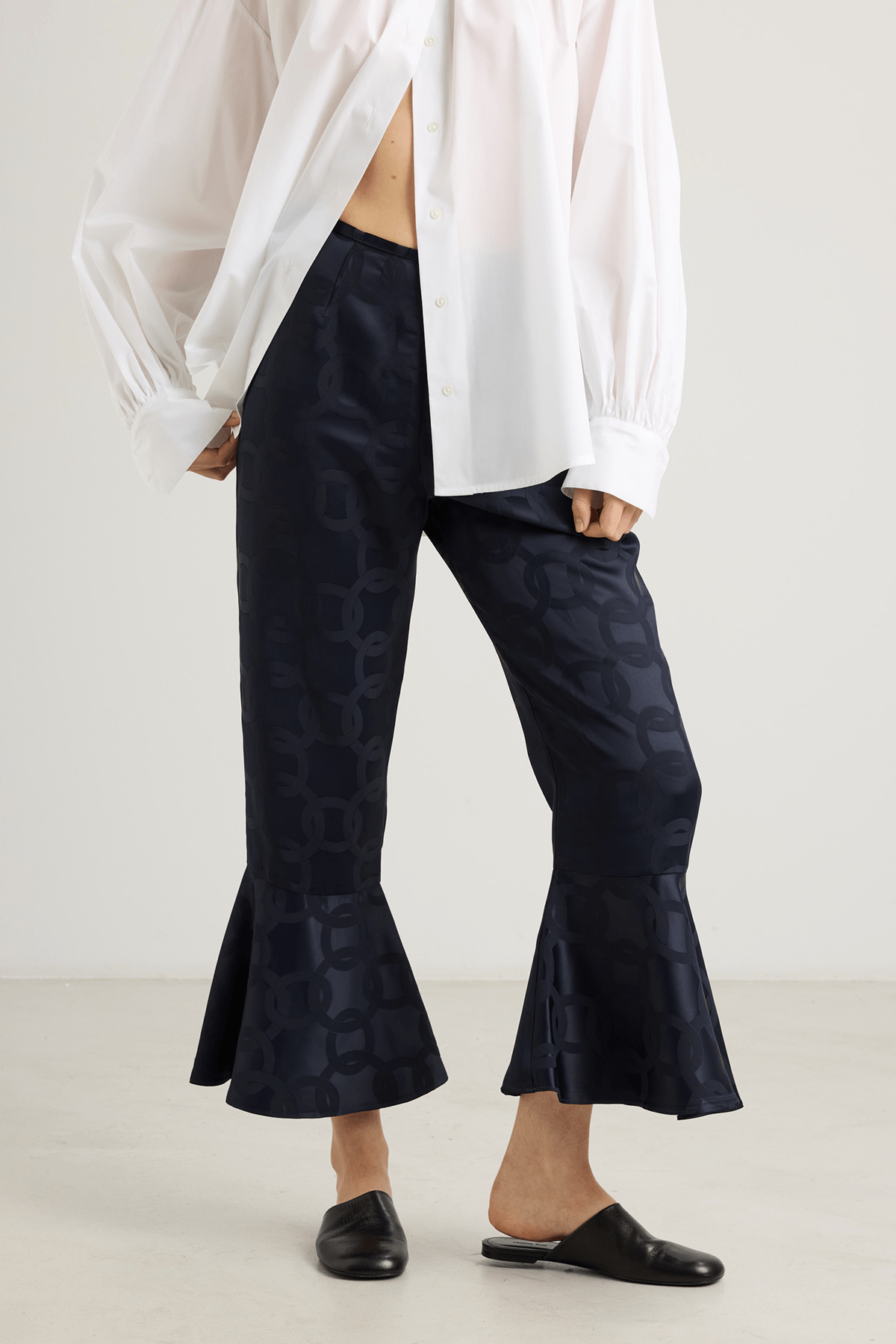 Model wearing Kasey trousers in dark blue satin jacquard with flounced hem.
