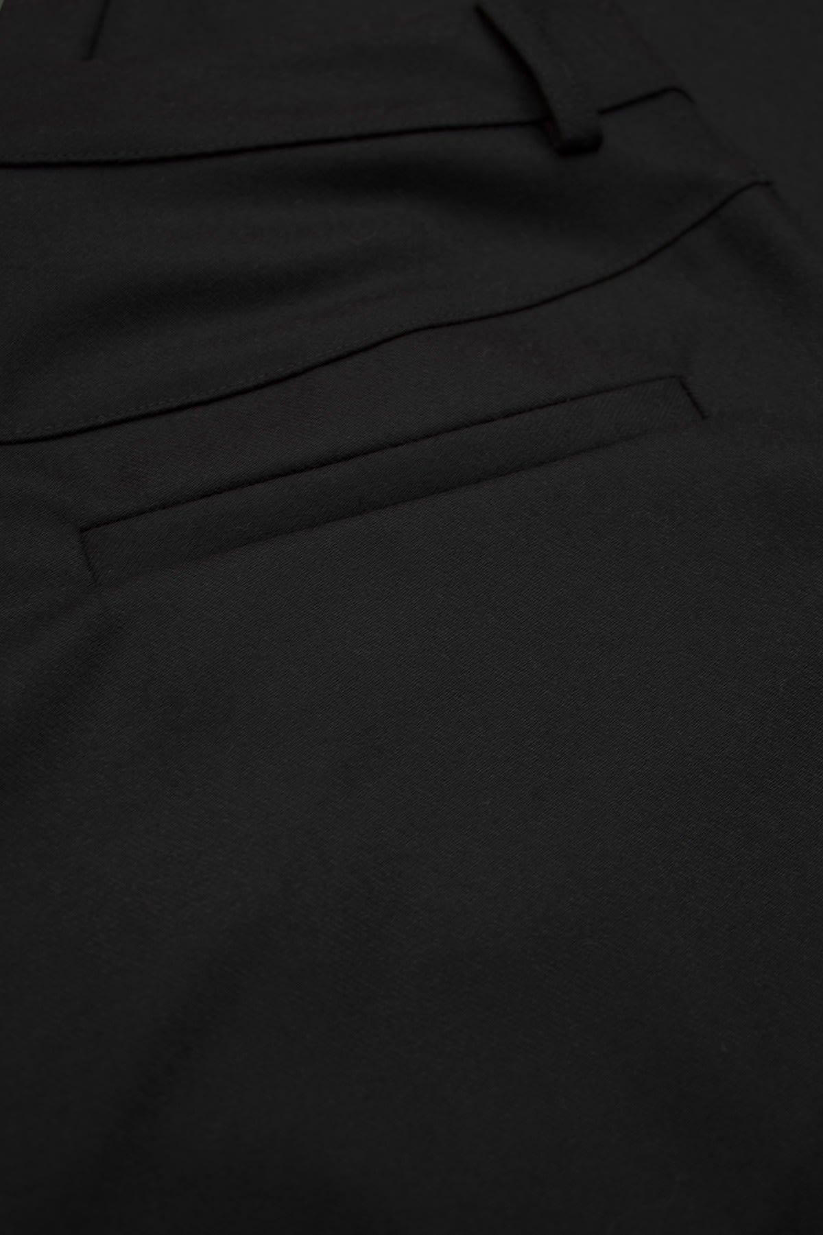 A refined view of the welt back pocket on the black barrel-leg trousers.