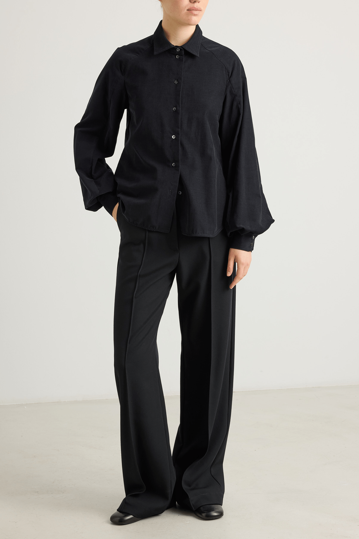 Model wearing Kosta trousers in black wool suiting with structured wide leg.
