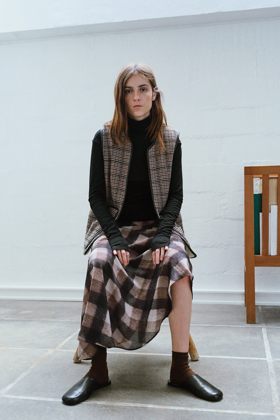 Girl in a vest and a checked skirt, shitting on a chair in a hall