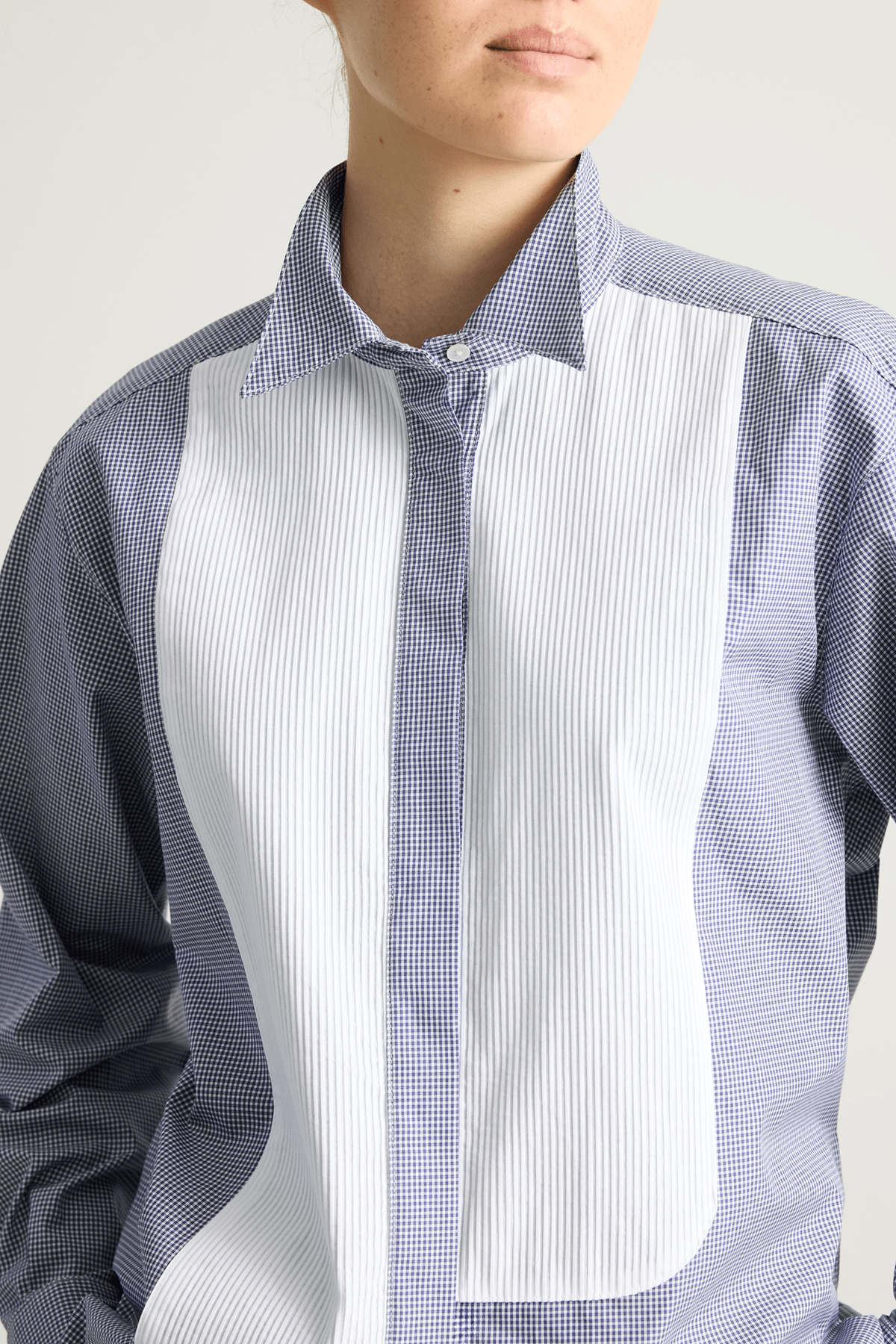Model wearing blue check Tuxedo shirt with pleated asymmetrical bib and stand collar.