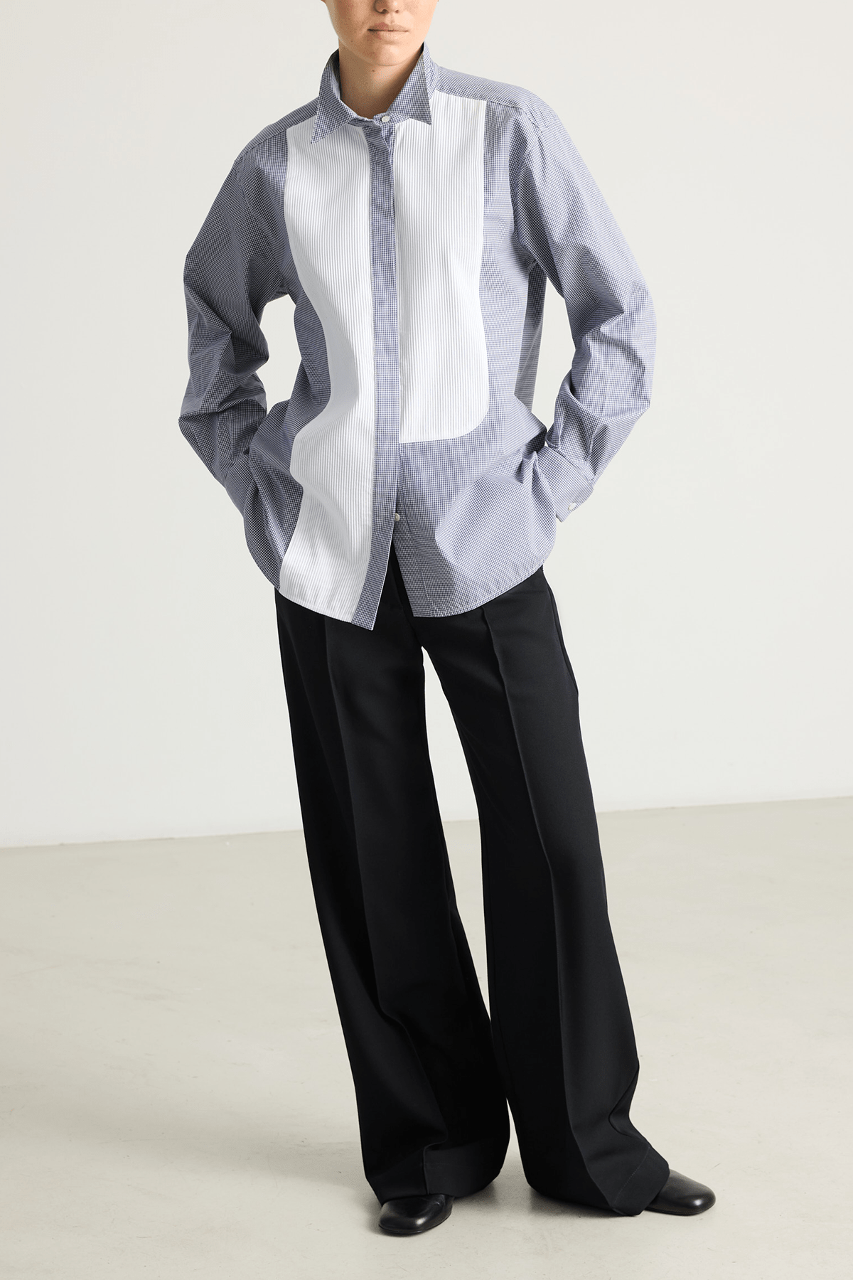 Model wearing a blue check Tuxedo shirt with pleated asymmetrical bib and stand collar.