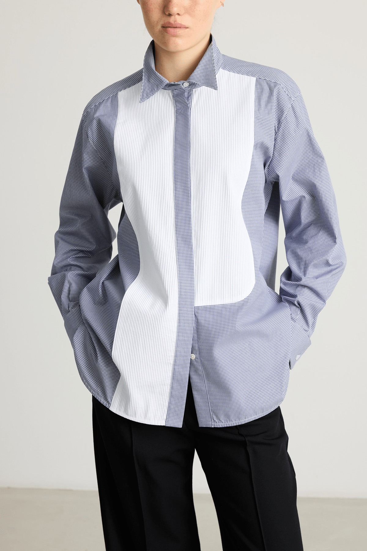 Model wearing a blue check Tuxedo shirt with pleated asymmetrical bib and stand collar.