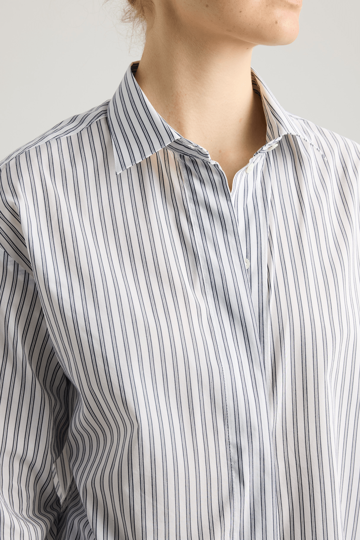 Model wearing Vega shirt in white cotton with grey stripes and elongated cuffs.