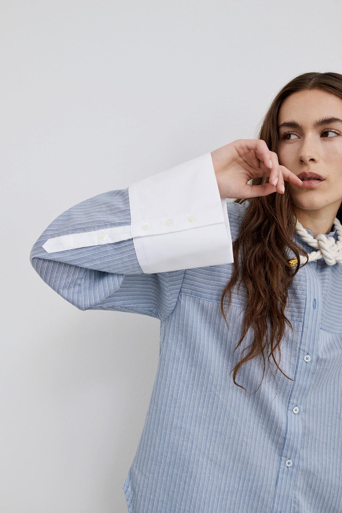 Model wearing Viola blue striped shirt with a blouse with wide sleeves, showcasing its contrasting cuffs.