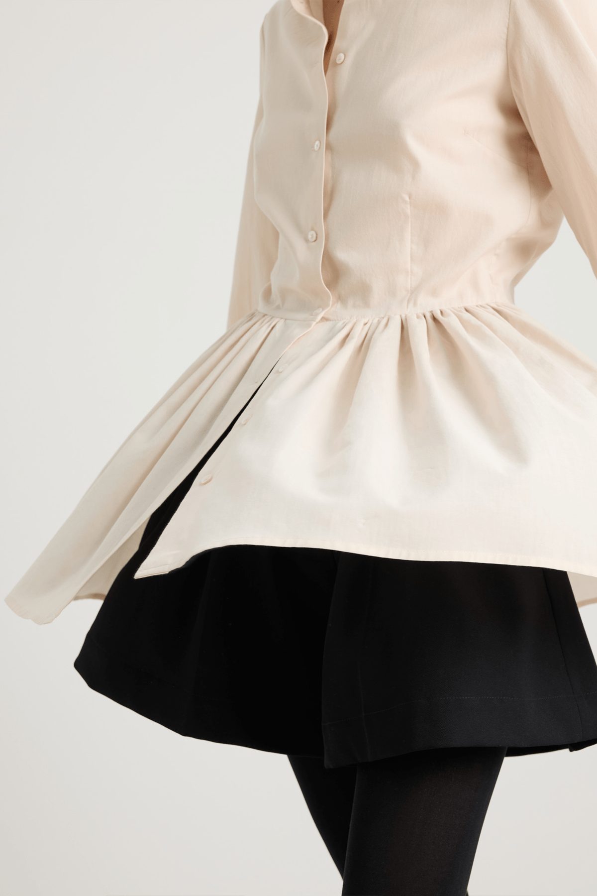 girl wearing Cream long-sleeved mini dress with, button-down front, and gathered peplum-style skirt.