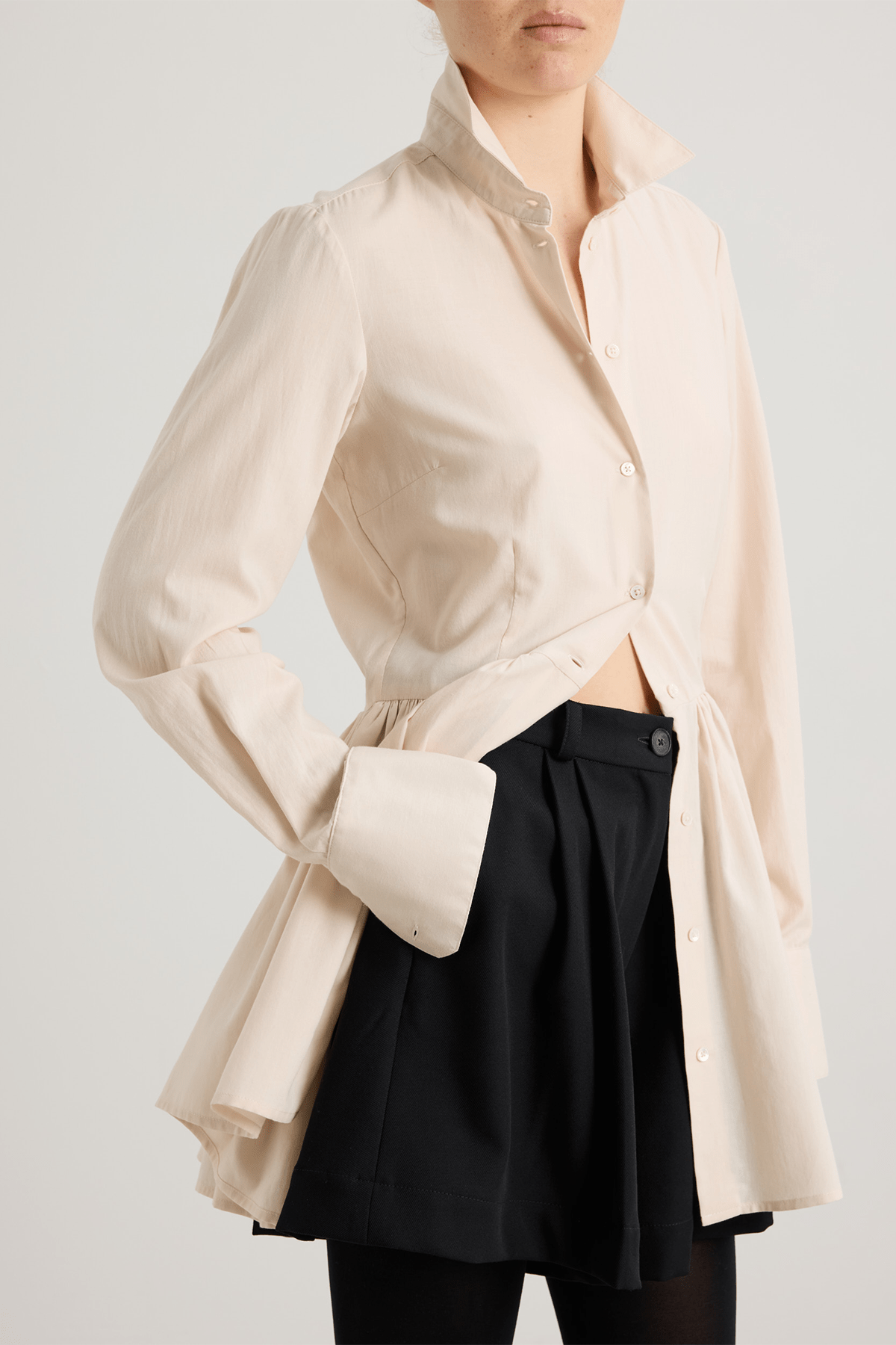 girl wearing Cream long-sleeved mini dress with, button-down front, and gathered peplum-style skirt.