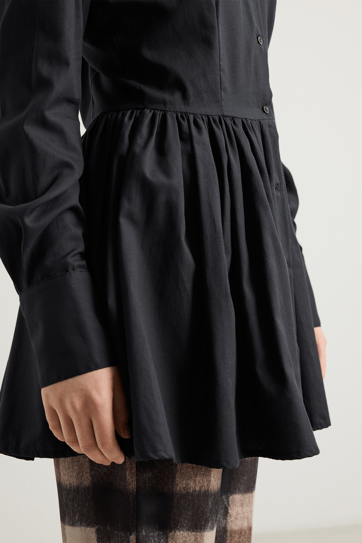 girl in Black long-sleeved mini dress with, button-down front, and gathered peplum-style skirt.