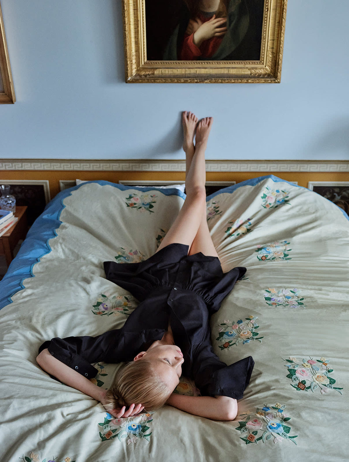 blonde girl laying on a bed in a bedroom wearing Black long-sleeved mini dress with, button-down front, and gathered peplum-style skirt.