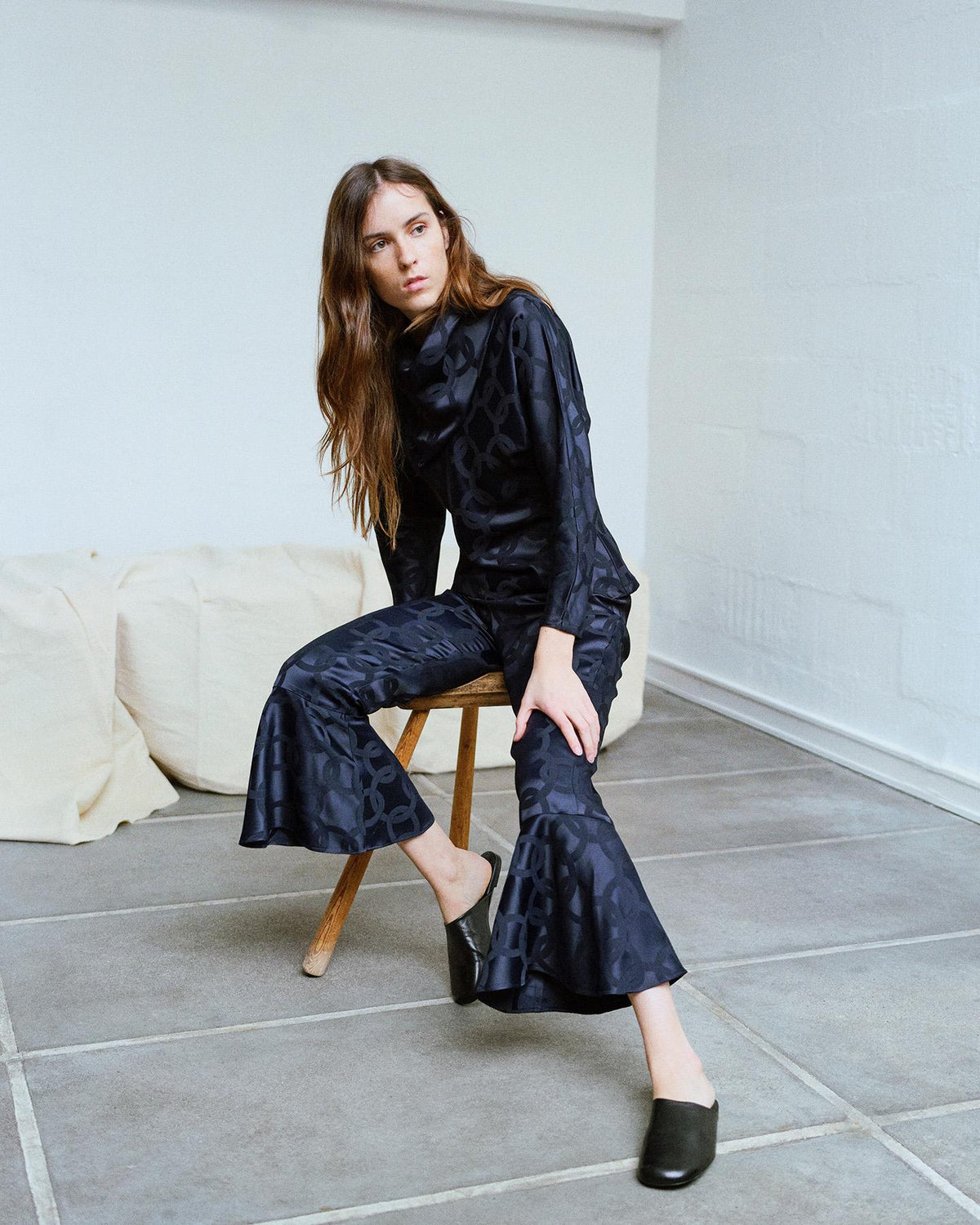 girl sitting on a chair in a black top and trousers in a subtle geometric jacquard pattern