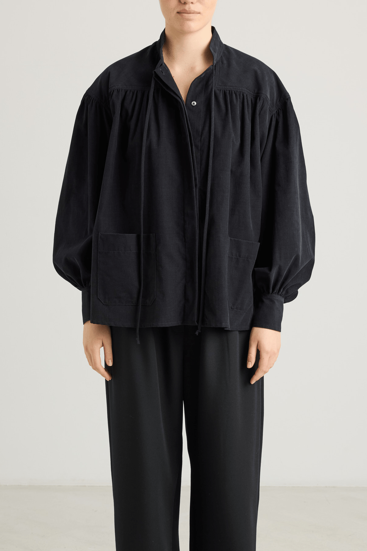 girl in black checked shirt with a tie-neck detail, front button closure, and long voluminous balloon sleeves gathered at the wrists.