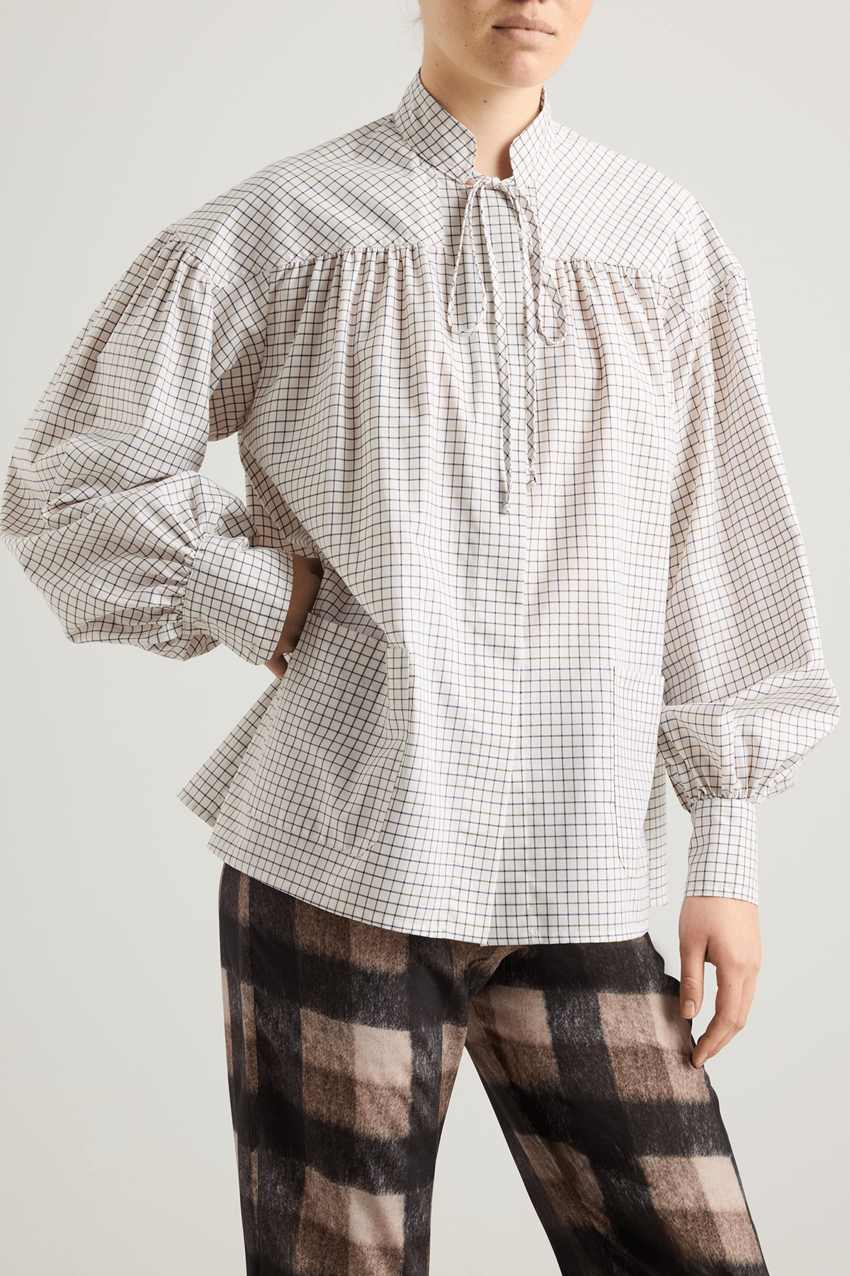 girl in White checked shirt with a tie-neck detail, front button closure, and long voluminous balloon sleeves gathered at the wrists.