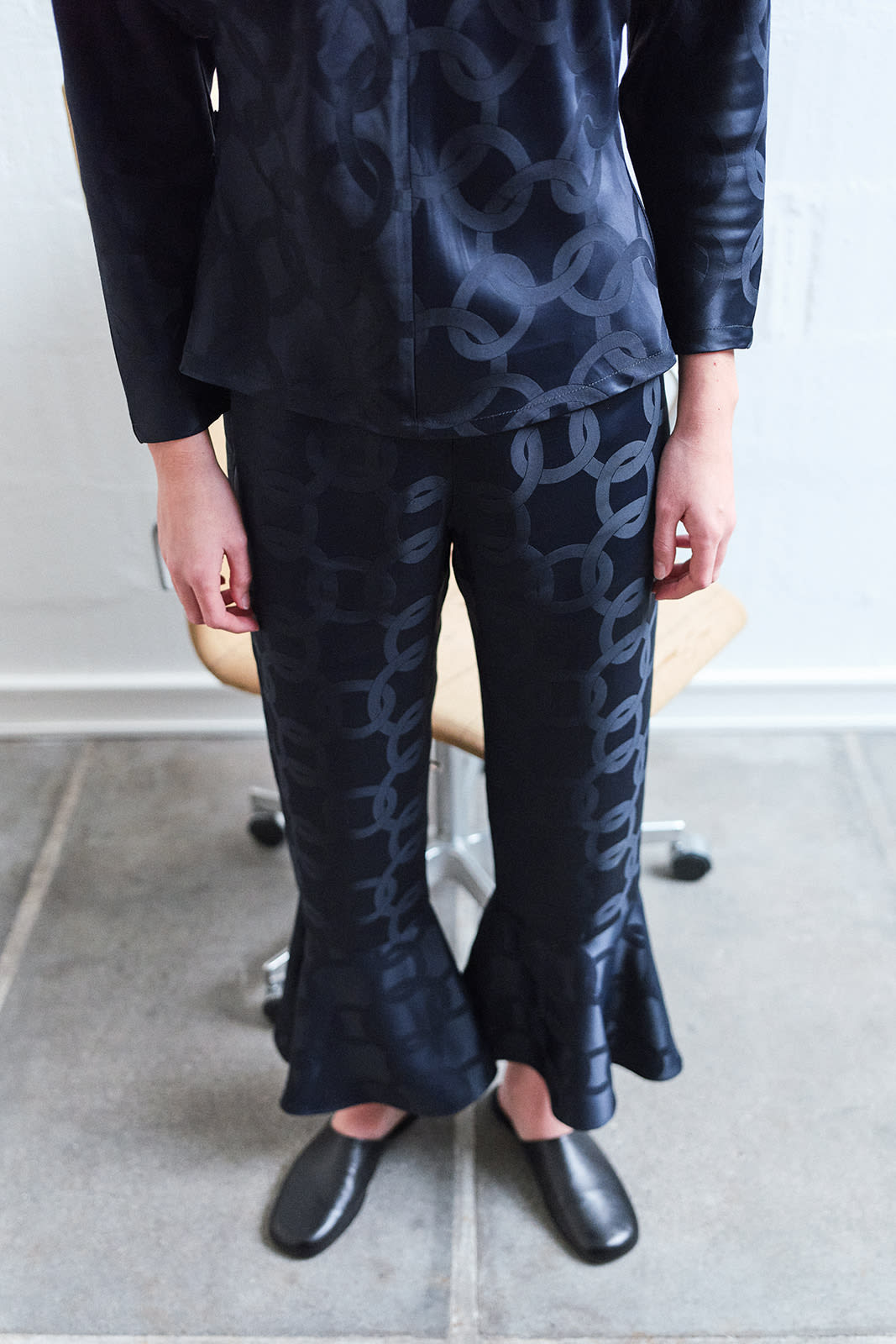girl in front of a chair in Checked flared pants with ruffled hems in black tones.