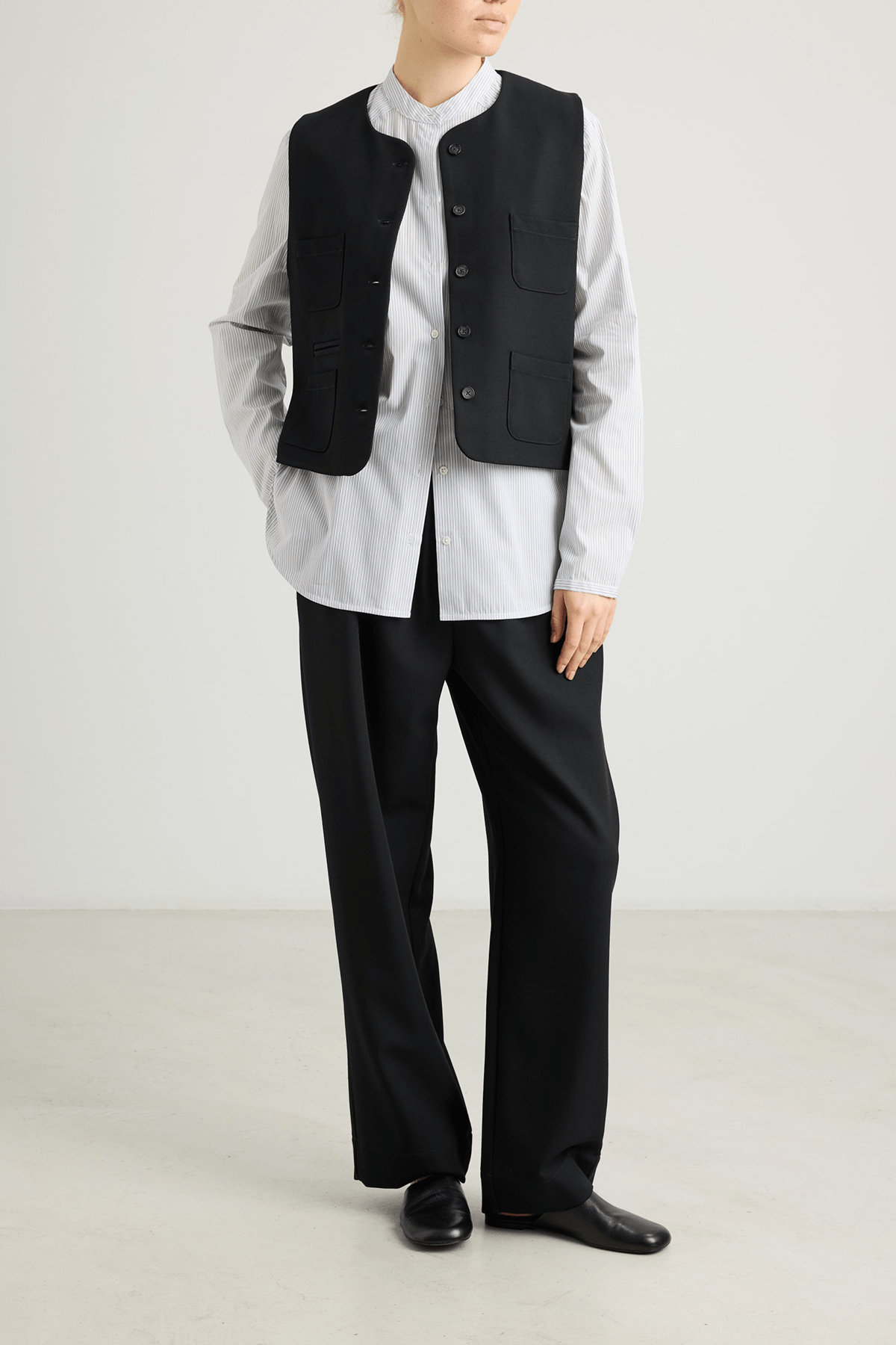 girl in black trousers, striped white button down and black vest