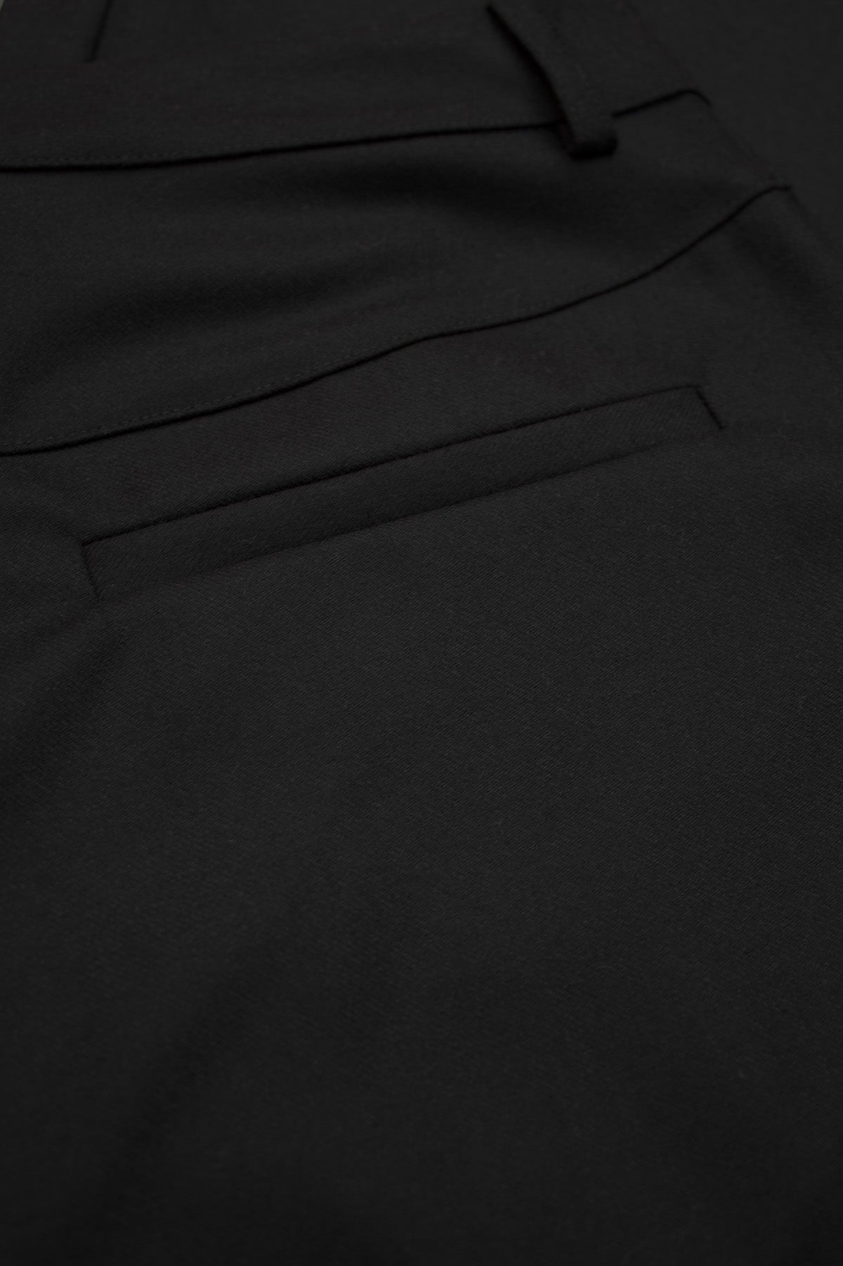 A refined view of the welt back pocket on the black barrel-leg trousers.