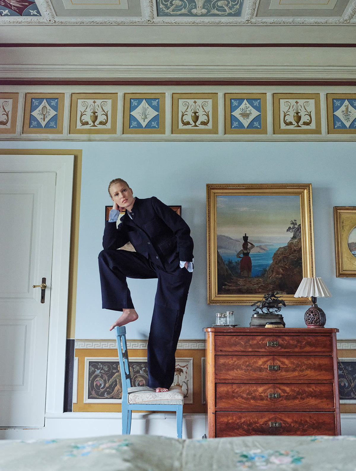 blonde girl standing on a chair in a lounge with navy short jacket on