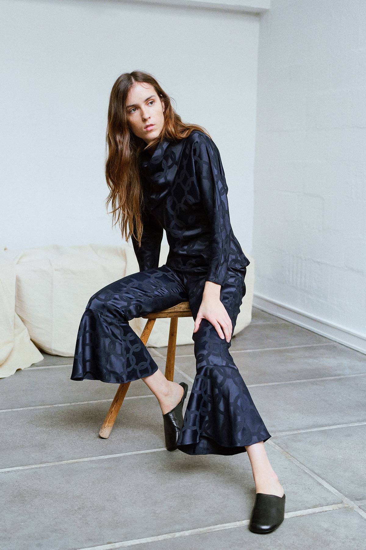 brunette girl in Checked flared pants with ruffled hems and blouse in black tones, sitting on a chair